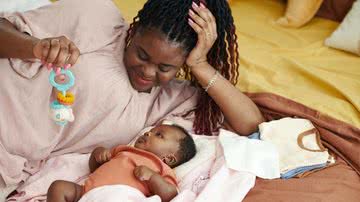 Mulher deitada ao lado de bebê recém nascido segura brinquedo para criança