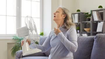 Mulher segura ventilador em frente ao corpo, demonstrando estar com calor excessivo