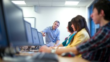 Jovens em frente a letas de computador com professor ao fundo