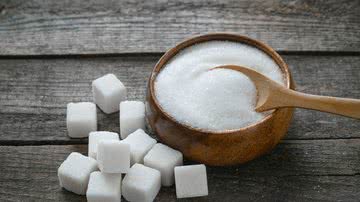 Cubos de açúcar ao lado de pote de açúcar