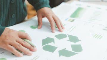 Mãos sobre cartaz com sinal gráfico que representa reciclagem de materiais