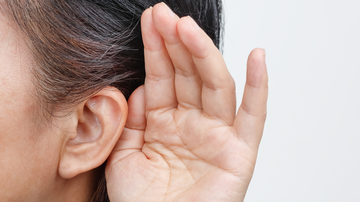 Mulher coloca mão ao redor da orelha como um sinal para tentar escutar melhor