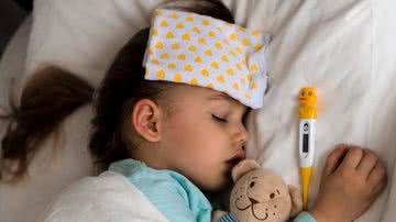 criança deitada com lenço na testa e termômetro ao lado