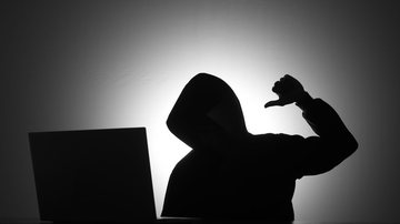 Silhueta de homem encapuzado com punho fechado em frente a computador