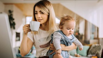 Mãe segura criança desajeitadamente enquanto toma café