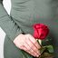 Mulher de vestido segura rosa vermelha em frente às partes íntimas