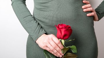 Mulher de vestido segura rosa vermelha em frente às partes íntimas