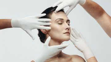 Quatro mãos com luvas cirúrgicas manipulam rosto de mulher