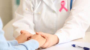 Médica com fita do outubro rosa acolhe paciente segurando suas mãos